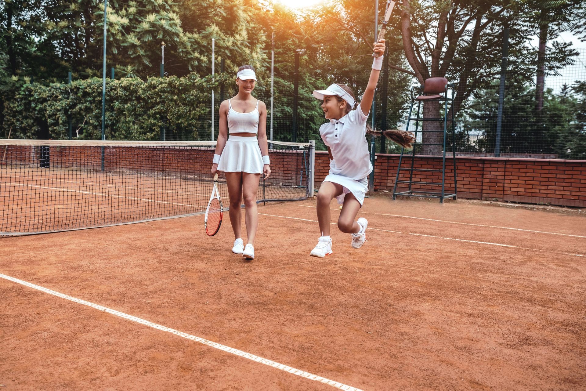 Happy little winner! Full length shot of two sporty girls in tennis club. Happy child having fun on tennis court with woman tennis player. Exercises outdoors