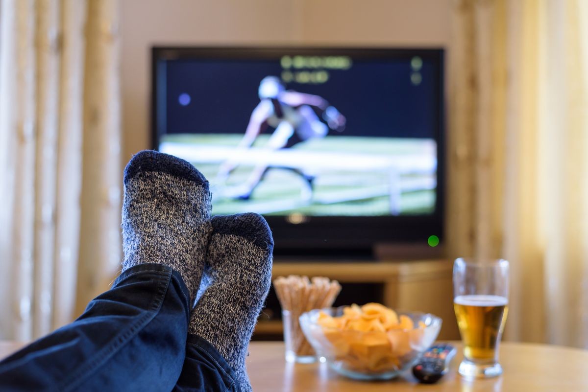 Watching tennis match on TV set (television) with feet on table and eating snacks  stock photo